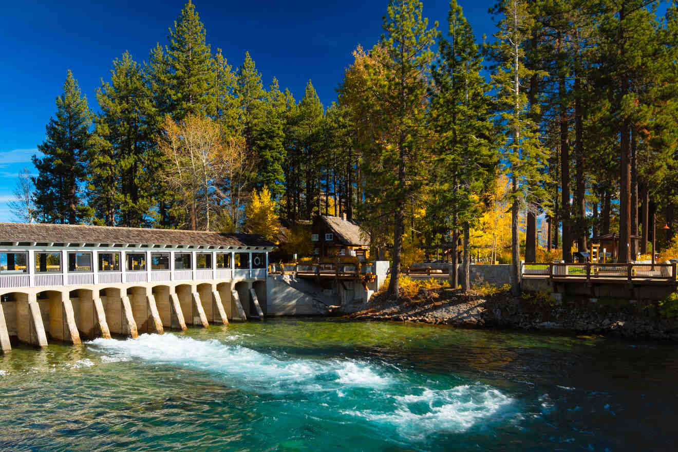 Picturesque riverside scene with a flowing stream, pedestrian bridge, and surrounding autumn trees.